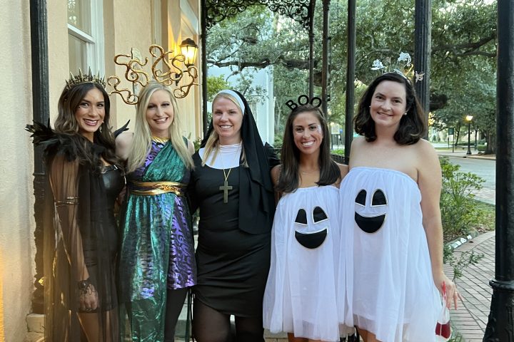 Five people in costume pose on a brick patio with trees and a building.