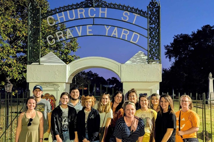 Group of people posing in front of 'Church St Grave Yard' gate at dusk.