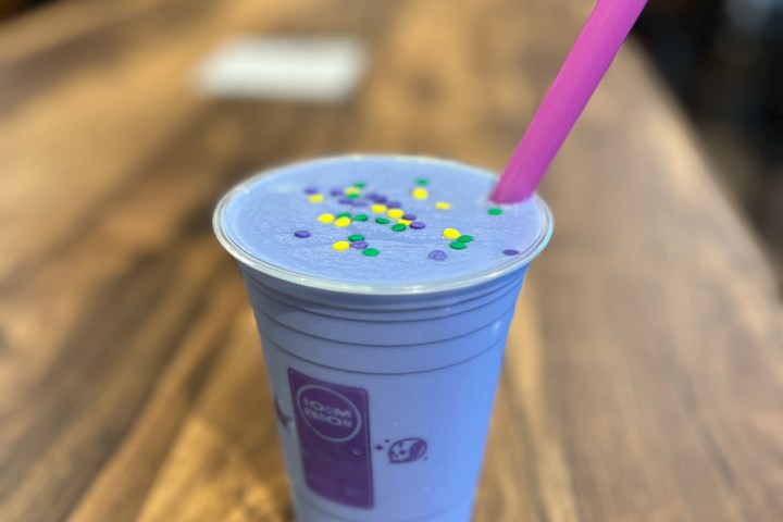Purple drink with sprinkles and pink straw on a wooden table.