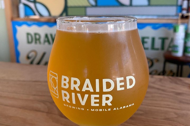 Glass of beer on wooden surface with colorful tap handles in background.