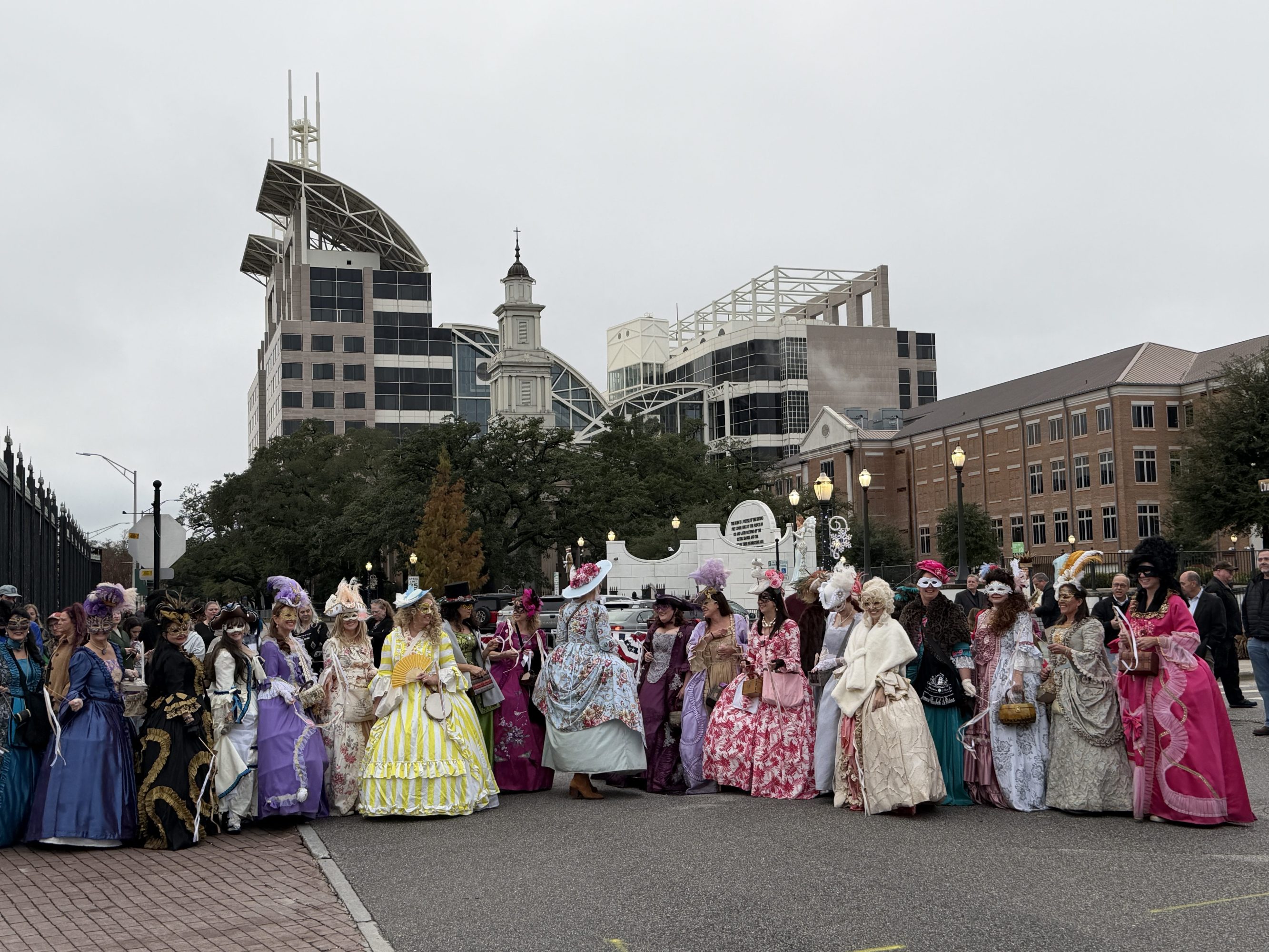 Group of people in colorful costumes with buildings in the background.