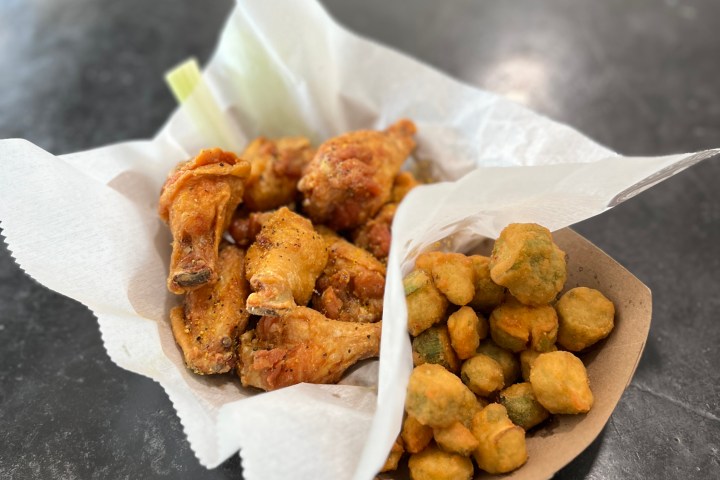Basket with fried chicken wings and fried okra on a dark table.