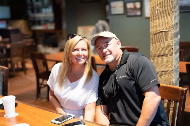 Smiling couple sitting at a table in a cafe, with a smartphone and cup in front.