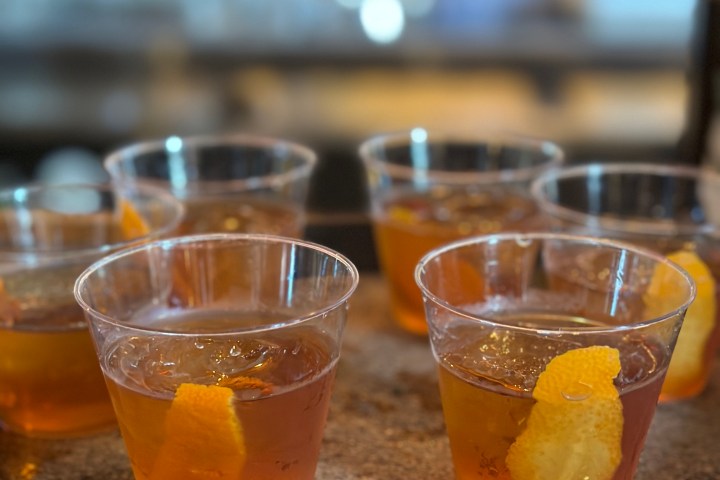 Tray of cocktails with orange garnishes in clear plastic cups.