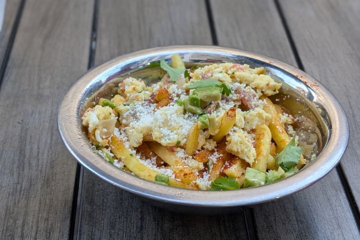 Pasta dish with vegetables and cheese in a silver bowl on a wooden table.