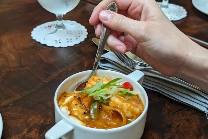 Hand holding spoon over soup bowl on wooden table with water glasses.