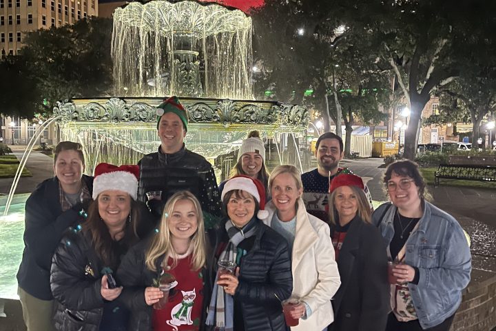 Group in festive attire poses at night in front of a lit fountain with city buildings in the background.