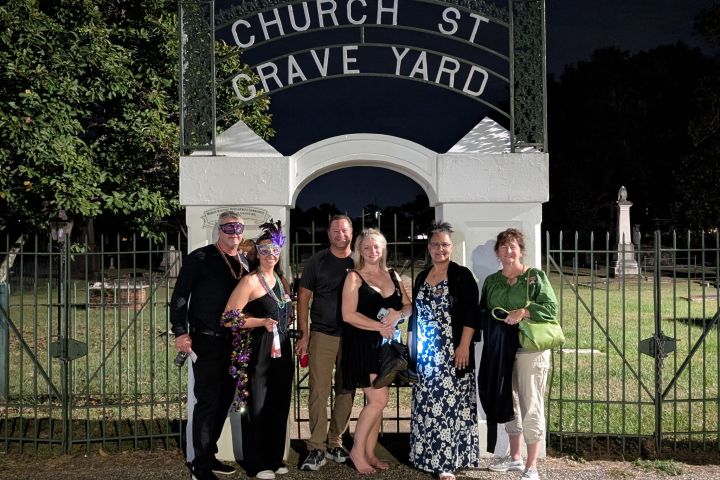 Six people in costumes stand under a 'Church St Grave Yard' sign at night.