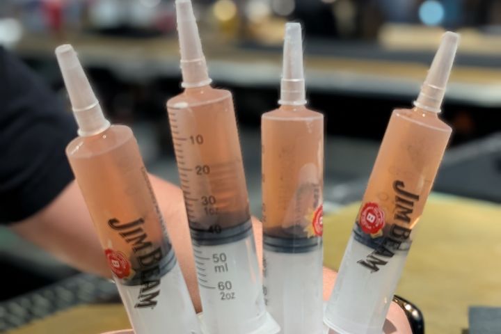 Four large syringes filled with orange liquid, held in a person's hand.
