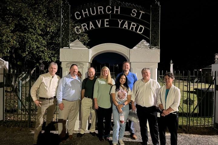Group of people posing at night under 'Church St Grave Yard' entrance sign.