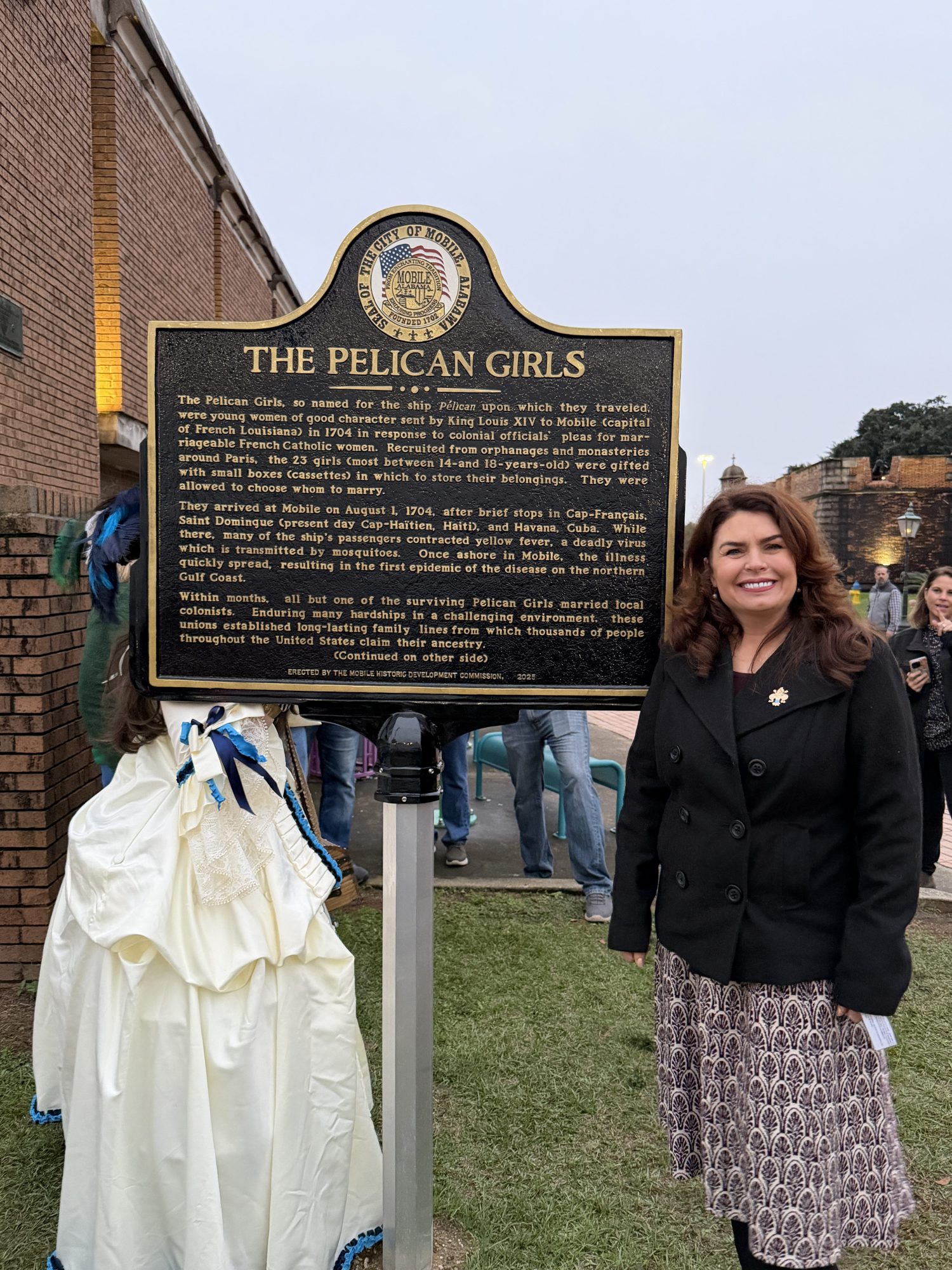 Woman stands next to a historical marker titled 'The Pelican Girls'.